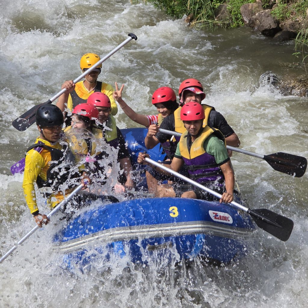 Guests in helmets paddling a blue raft through whitewater rapids in Phang Nga