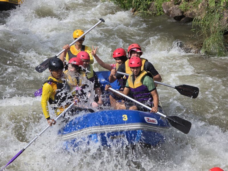 Guests in helmets paddling a blue raft through whitewater rapids in Phang Nga