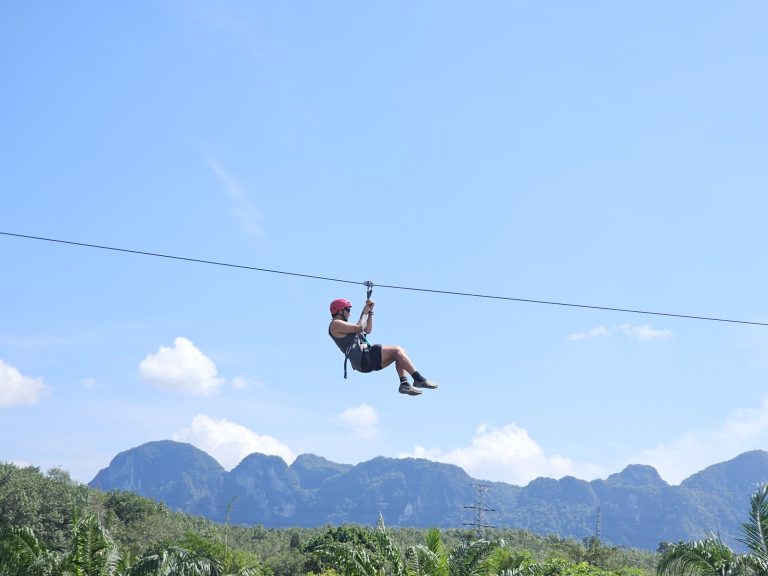 Zipline rider flying over green countryside with limestone mountains behind