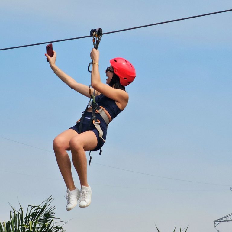 Smiling zipline rider in a red helmet taking a selfie on the line