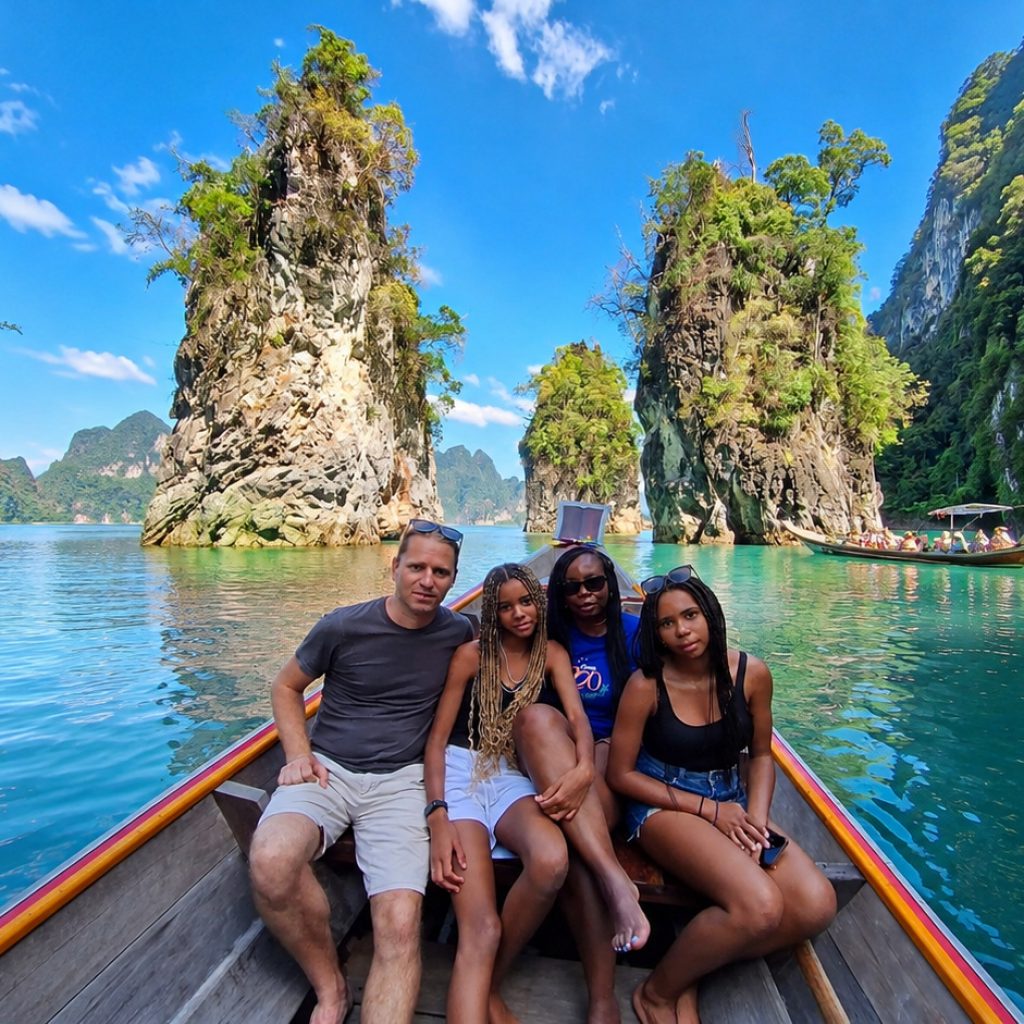 Guests sitting on a longtail boat in front of tall limestone rock towers on the emerald water of Cheow Lan Lake