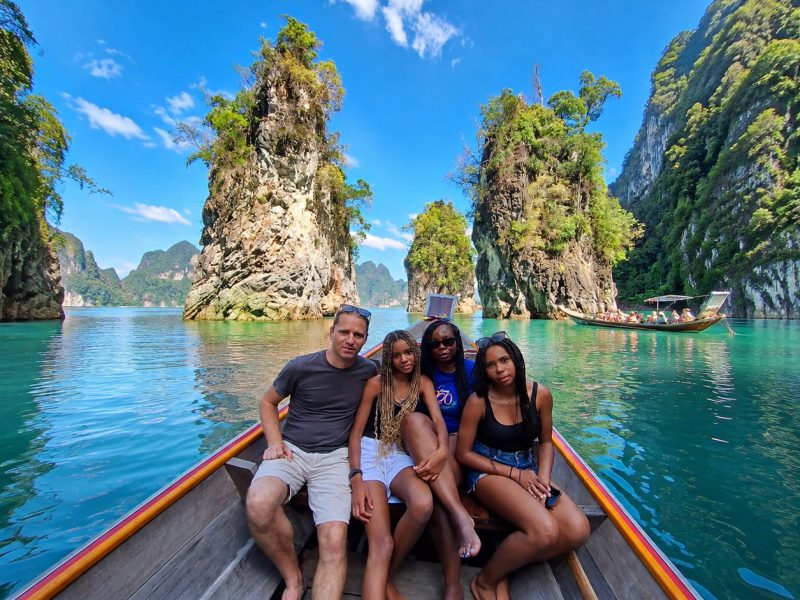 Guests sitting on a longtail boat in front of tall limestone rock towers on the emerald water of Cheow Lan Lake
